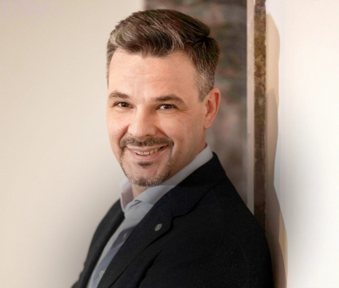 Markus Hauken - Professionelles Porträt eines lächelnden Mannes in dunklem Sakko und weißem Hemd vor neutralem Hintergrund.